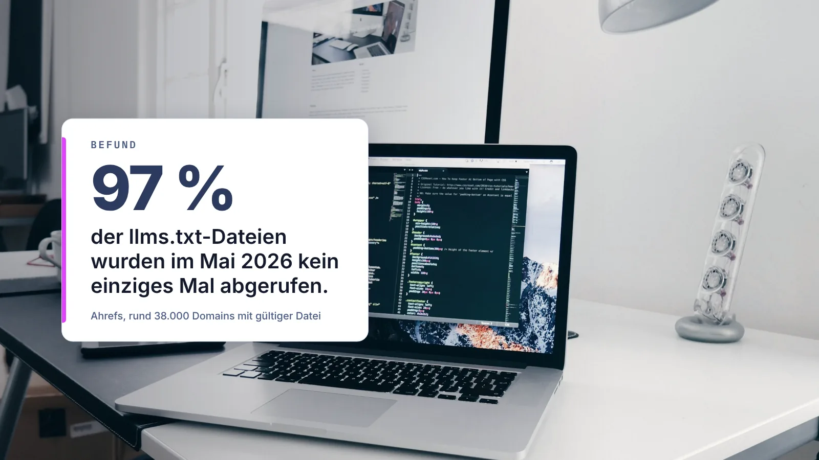 Aufgeklappter Laptop mit Quellcode auf einem Schreibtisch; eingeblendeter Befund: 97 % der llms.txt-Dateien wurden im Mai 2026 kein einziges Mal abgerufen (Ahrefs)
